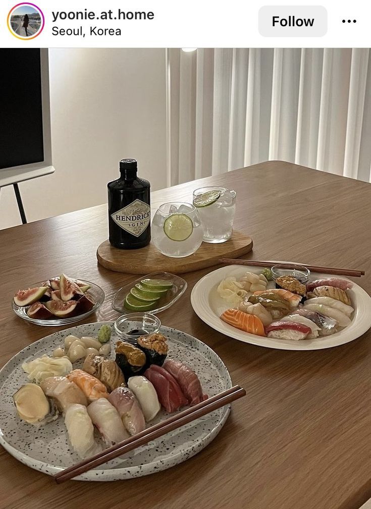 two plates with sushi and chopsticks sit on a table next to a bottle of booze