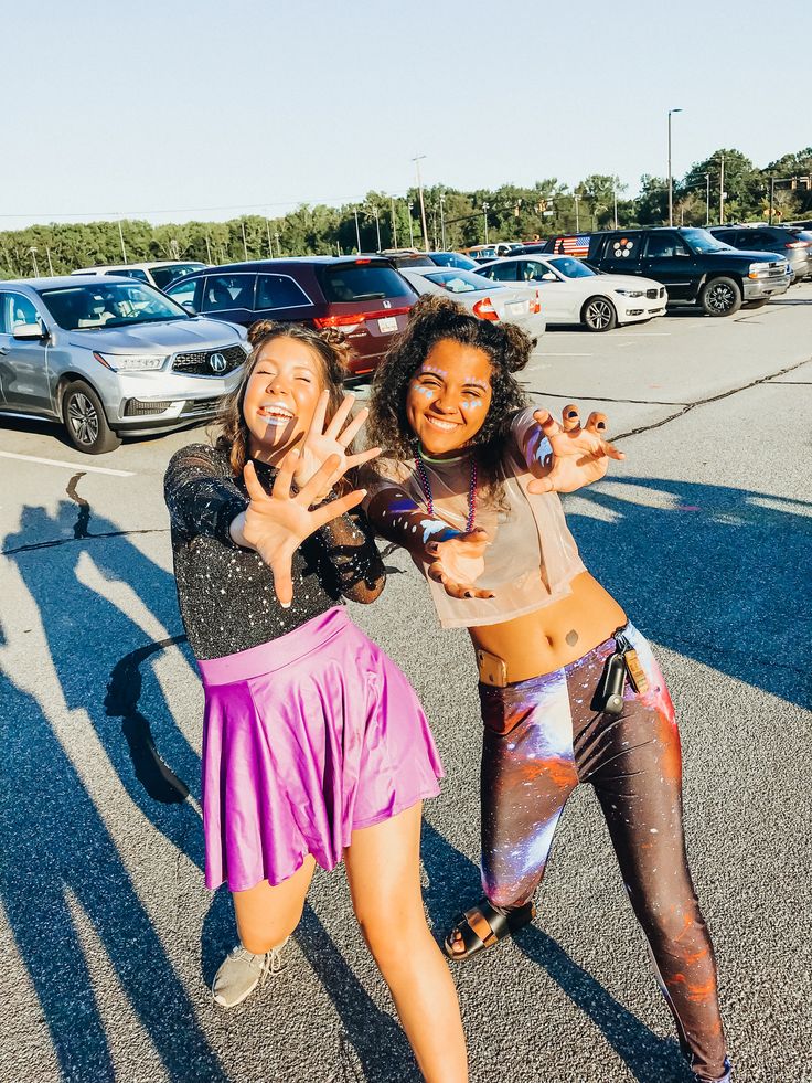 two young women are dancing in the parking lot with their hands up and one has her face painted