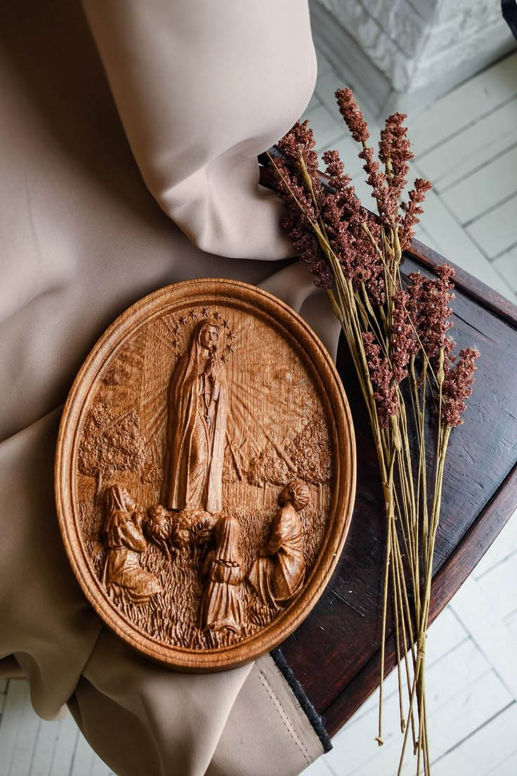 a wooden plate with a statue on it next to some dried flowers and a pillow