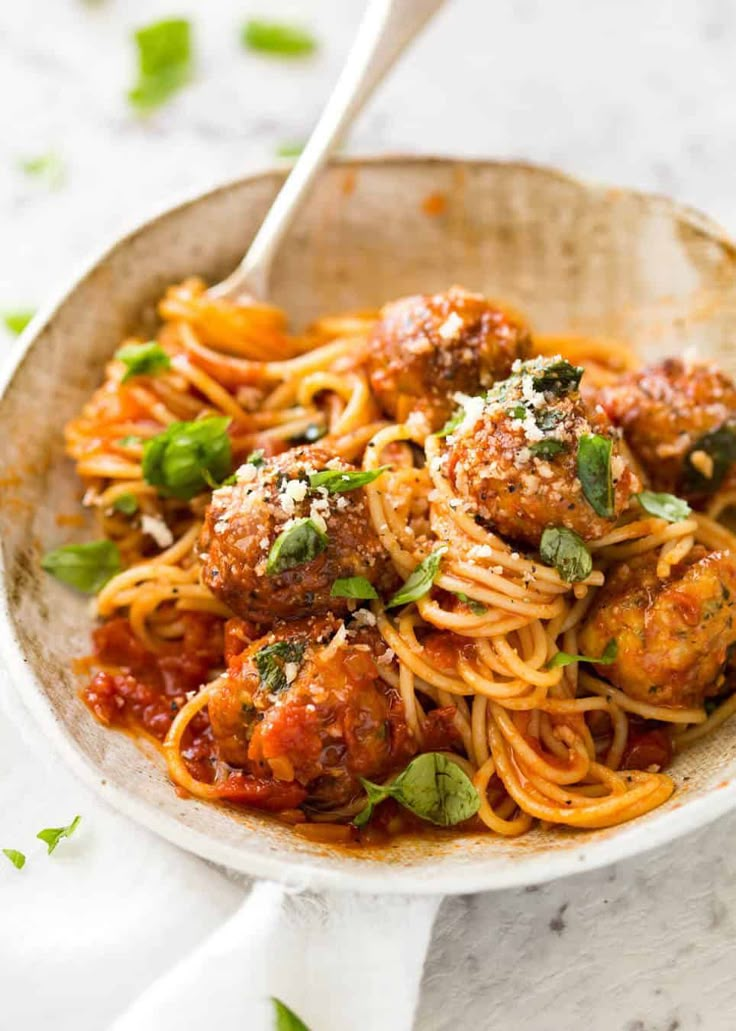 a bowl filled with spaghetti and meatballs on top of a white tablecloth next to a spoon