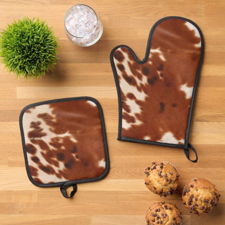 two oven mitts and some muffins on a wooden table next to a plant