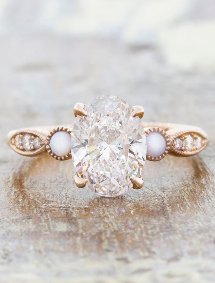 an oval shaped diamond ring with two pears on the band and a side stone