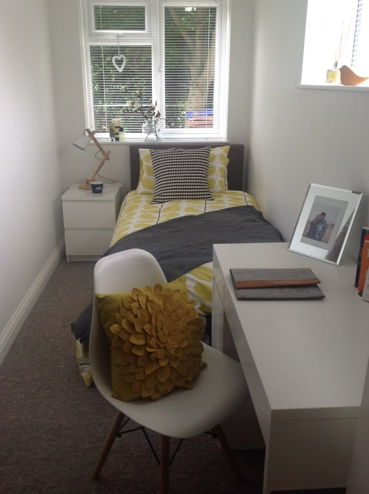 a bed room with a neatly made bed next to a white desk and chair in front of a window