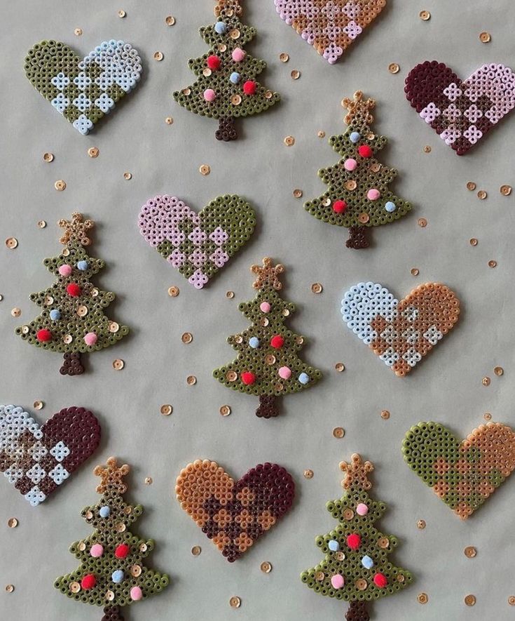 cross stitch christmas tree ornaments are displayed on a sheet of white paper with gold sequins