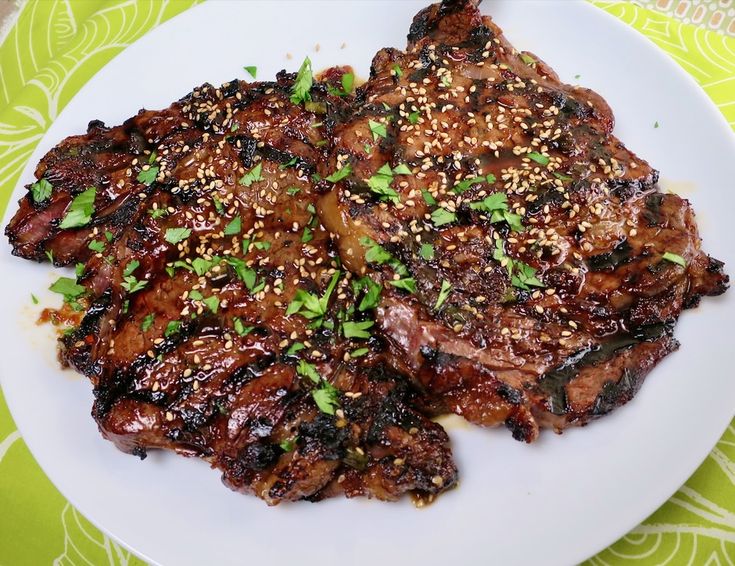 two pieces of meat on a white plate with sesame seeds and green garnish