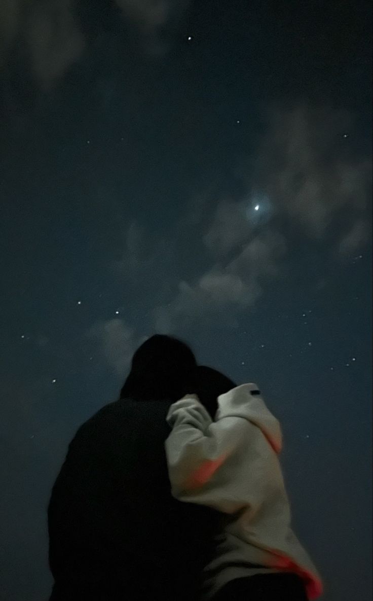 two people are looking up at the stars in the night sky with their arms around each other