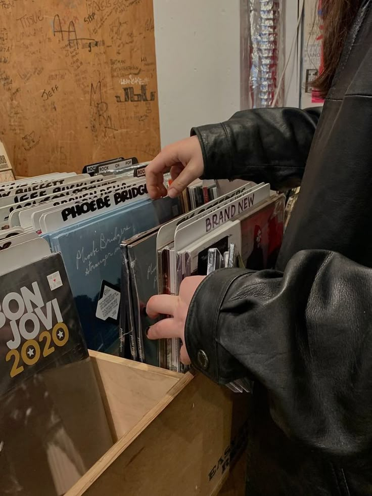 a person holding several records in their hands while standing next to some other cds on display