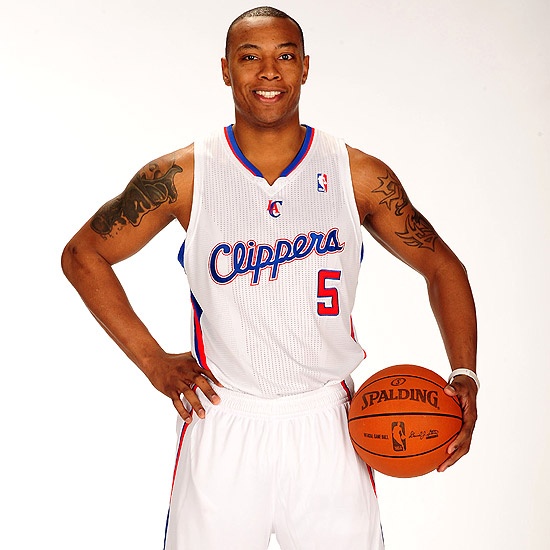 a man with tattoos holding a basketball in front of a white background and posing for the camera