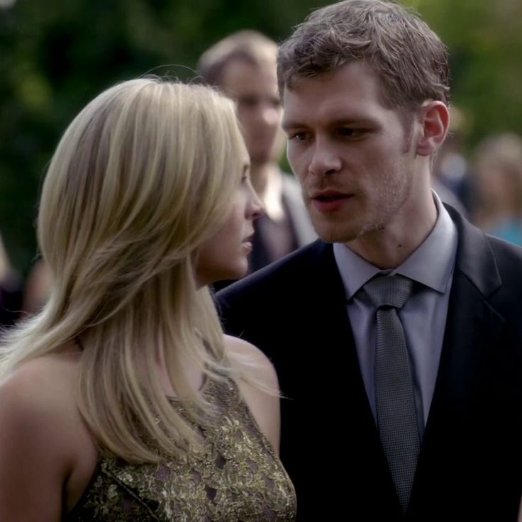 a man in a suit and tie standing next to a blonde woman wearing a gold dress