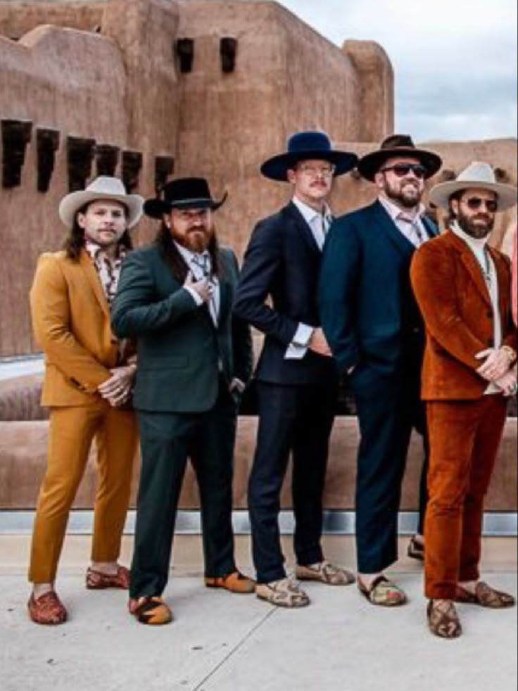 five men in suits and hats posing for a photo outside an adobe - style building