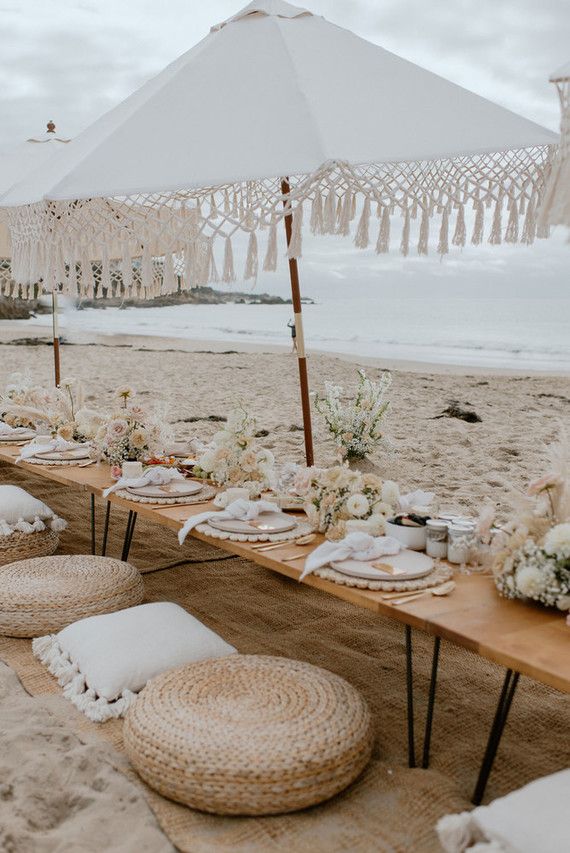 a table set up on the beach for an outdoor wedding reception with white flowers and tassels