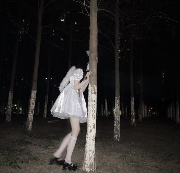 a woman dressed as an angel is leaning against a tree in the woods at night