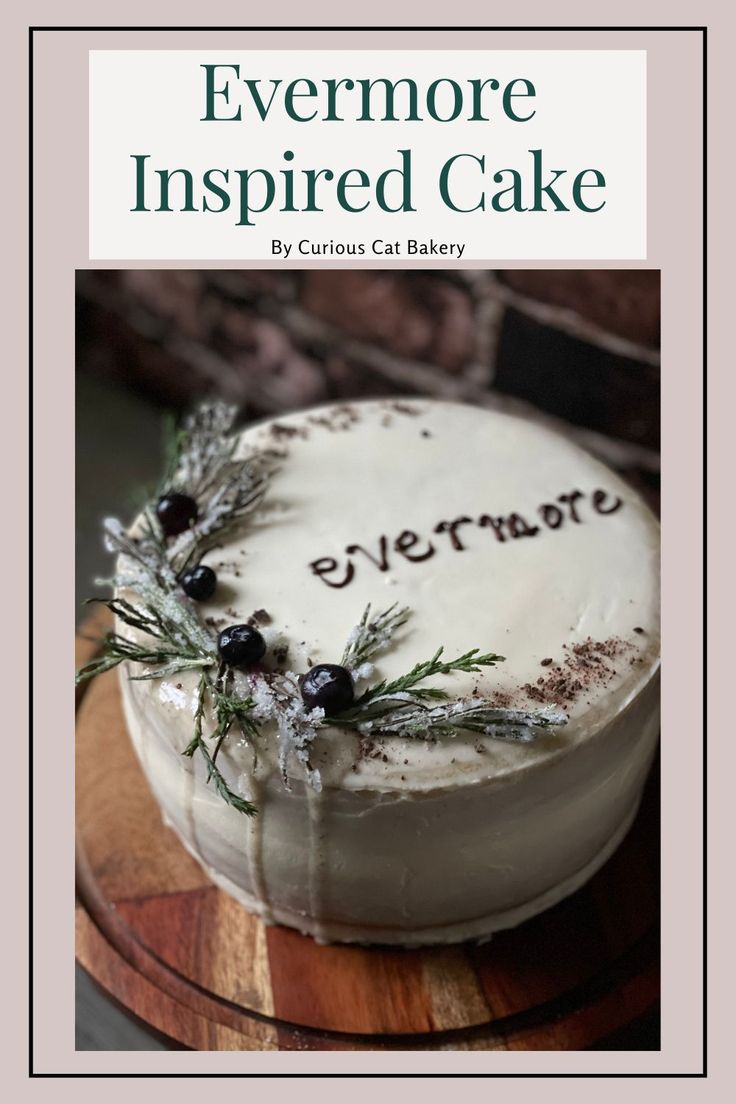 a white cake with frosting and greenery on top sitting on a wooden platter