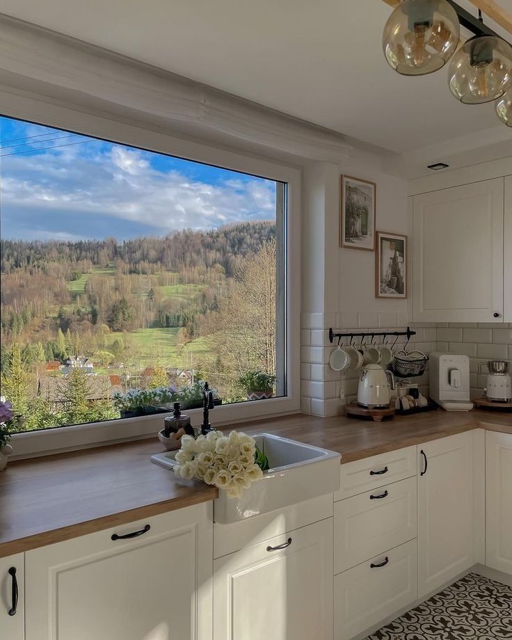 a kitchen with a large window looking out onto a valley outside the window and flowers on the counter