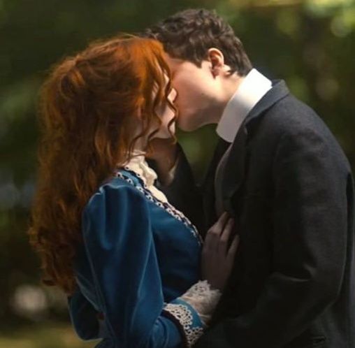 a man in a suit and tie kissing a woman with long red hair wearing a blue dress