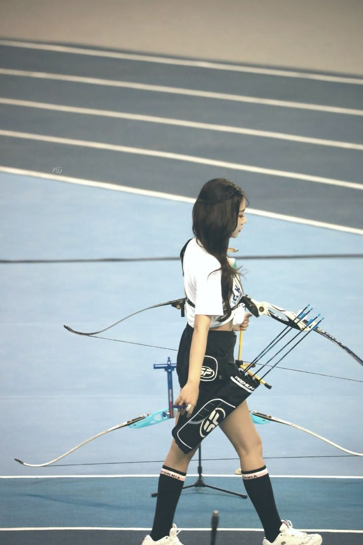 a woman holding a bow and arrows walking across a tennis court