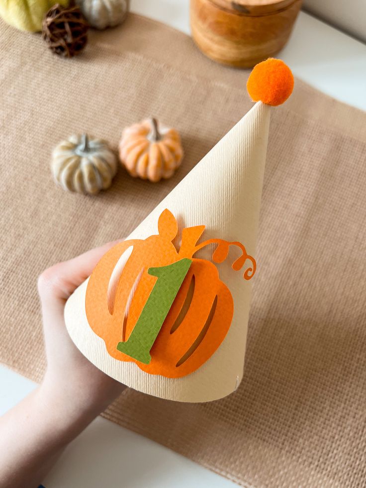 a hand holding a paper cone with a pumpkin on it and other decorations behind it