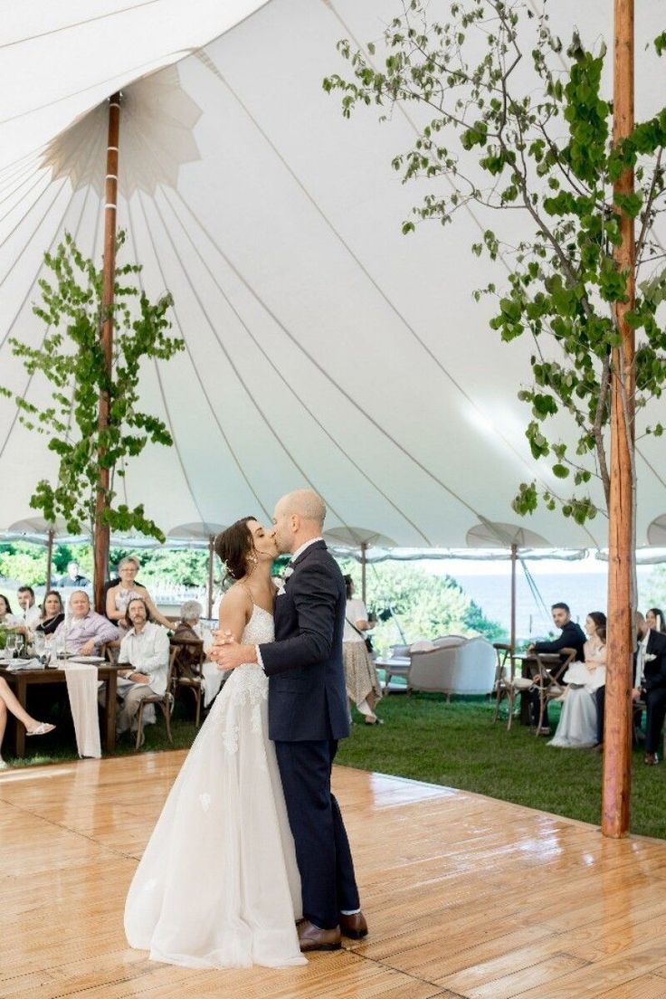 a bride and groom share their first dance under the tented area at an outdoor wedding reception