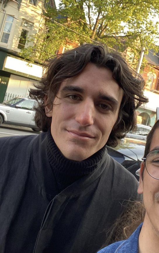 two people standing next to each other in front of parked cars on a city street