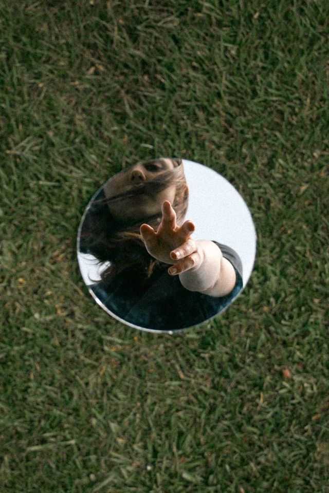 a woman's reflection in a mirror on the ground with her hand up to her face