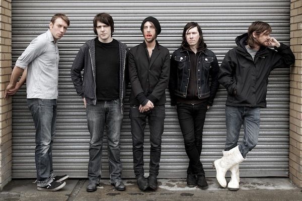 five people standing next to each other in front of a garage door with a white cat