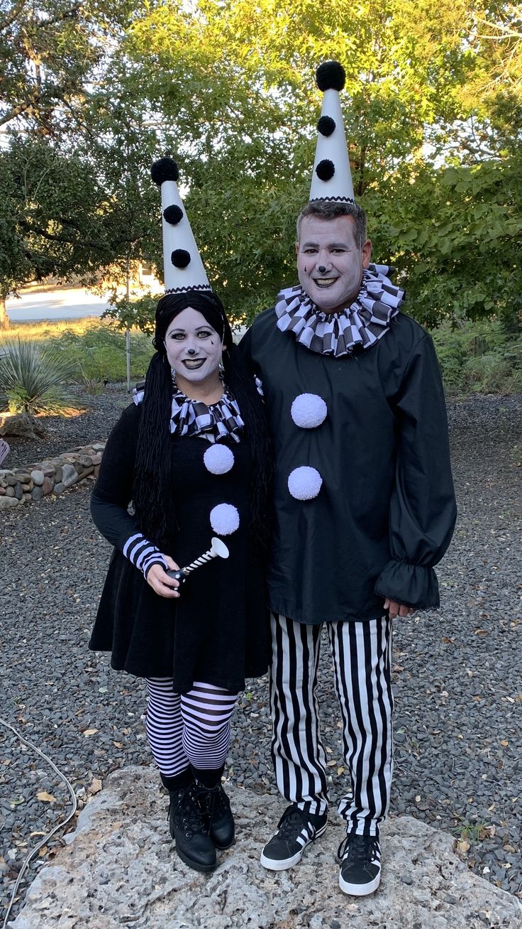 two people dressed up as clowns standing next to each other in front of trees