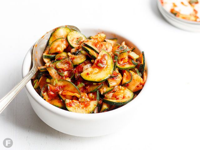 a white bowl filled with zucchini and sauce next to another bowl full of food