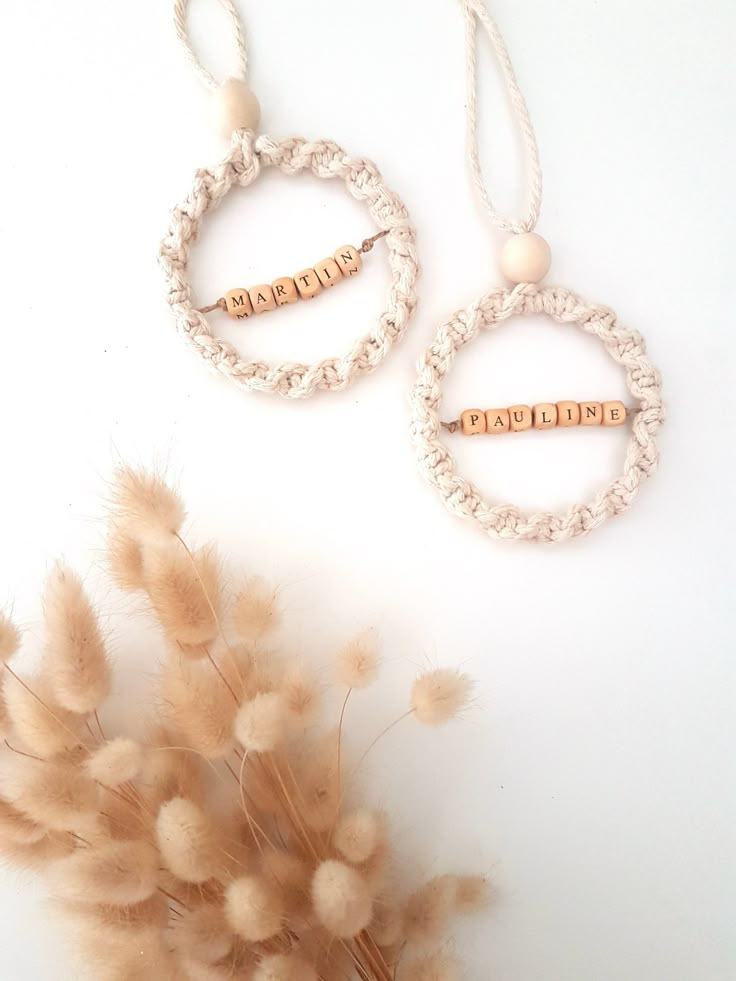 two pieces of jewelry sitting on top of a white table next to some dried flowers