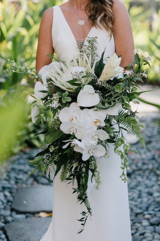 a woman in a white wedding dress holding a bouquet with greenery and flowers on it