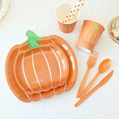 an orange pumpkin shaped paper plate next to utensils and cups on a white tablecloth