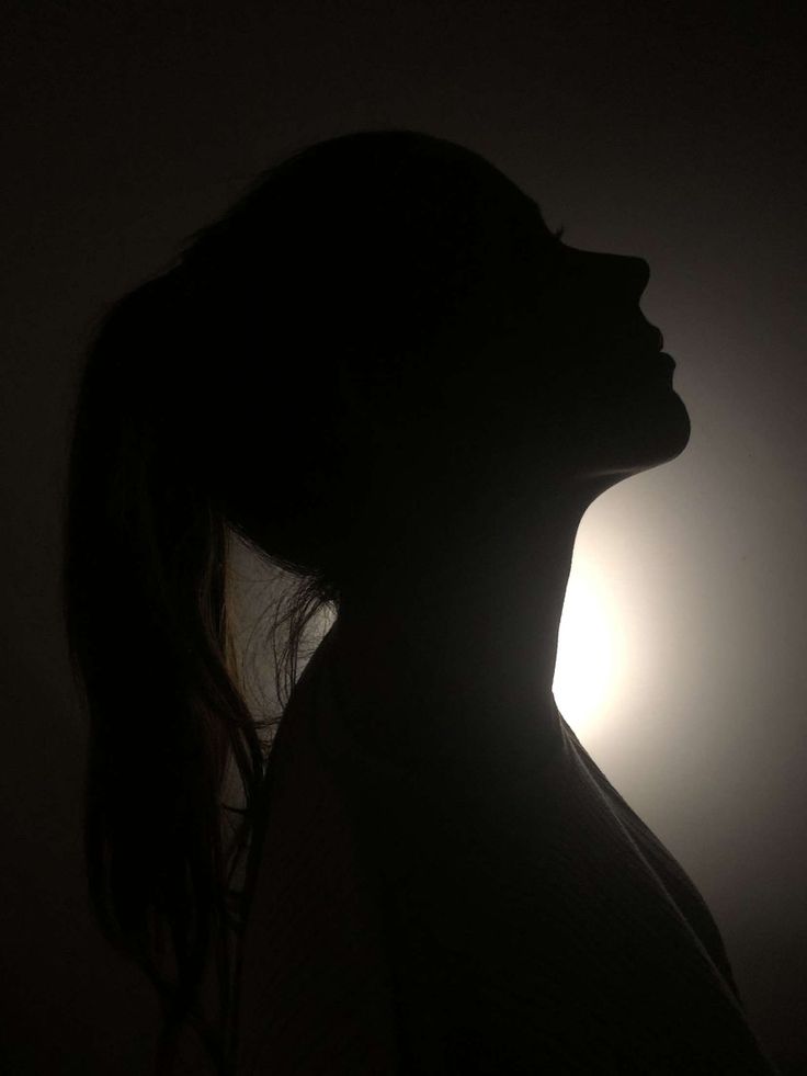 the silhouette of a woman's head with the sun shining behind her in the dark