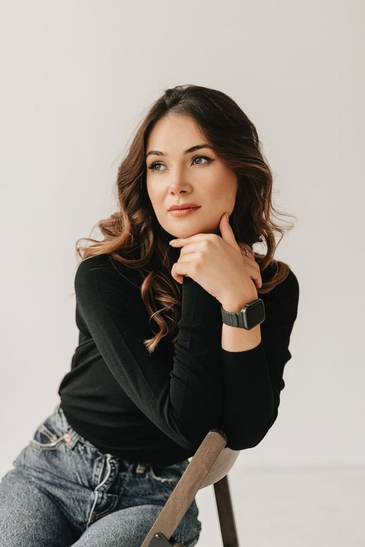 a woman is sitting on a chair with her hand under her chin and looking at the camera