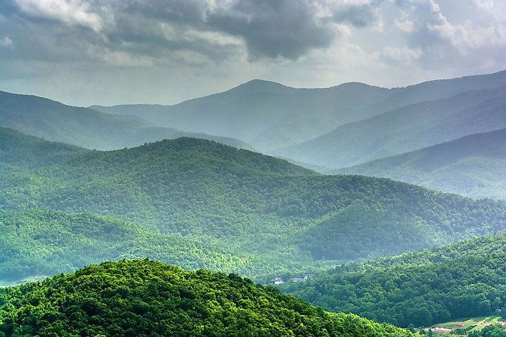 the mountains are covered with green trees and clouds in the distance, as seen from an overlook point