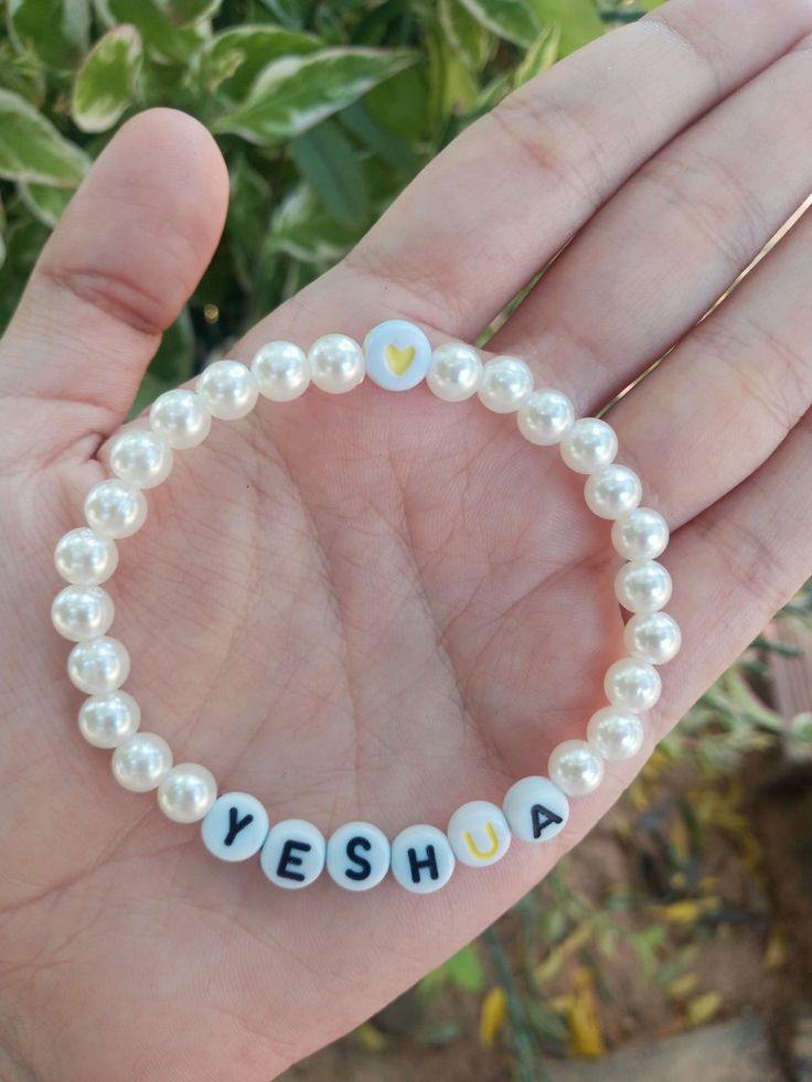 a hand holding a white beaded bracelet with the word yesha written on it