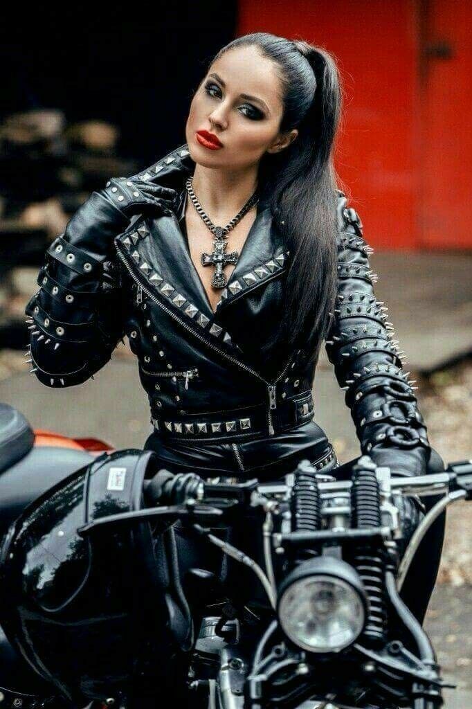 a woman sitting on top of a motorcycle wearing black leather clothes and studded gloves