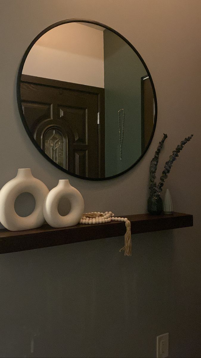 two white vases sitting on a shelf in front of a round mirror above it