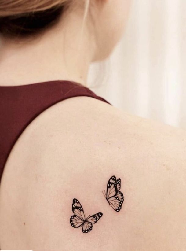 two butterflies tattoo on the back of a woman's shoulder