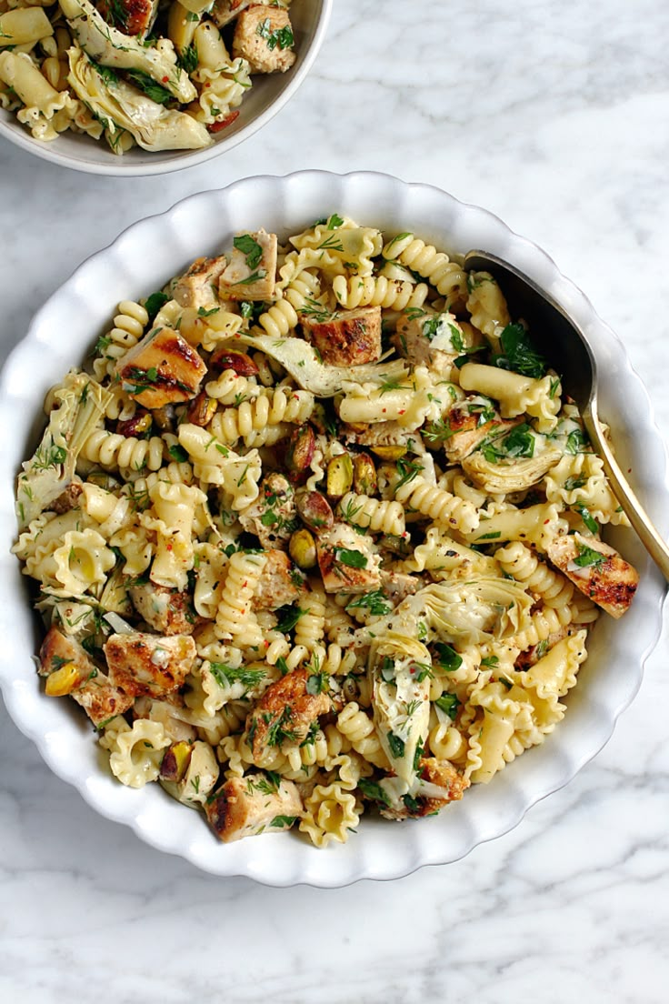 two bowls filled with pasta salad on top of a white table next to each other