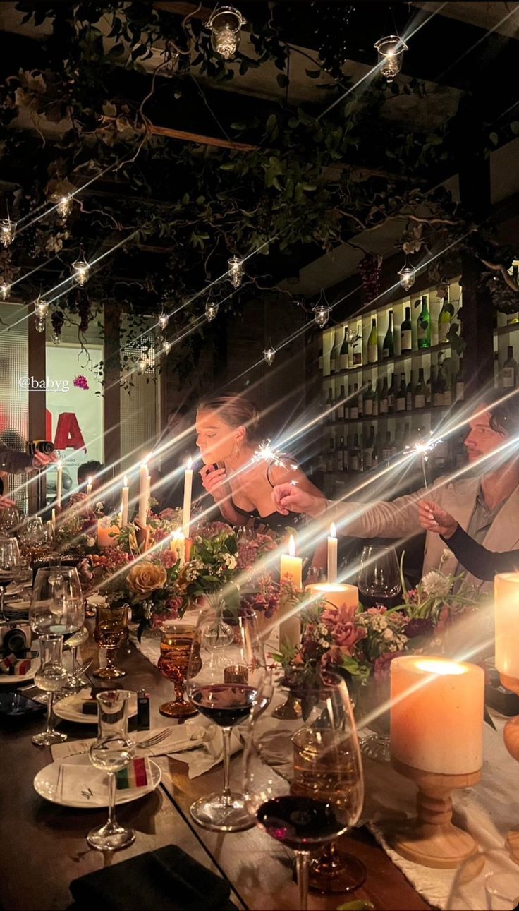 a long table is set with candles and flowers in front of the woman standing behind it