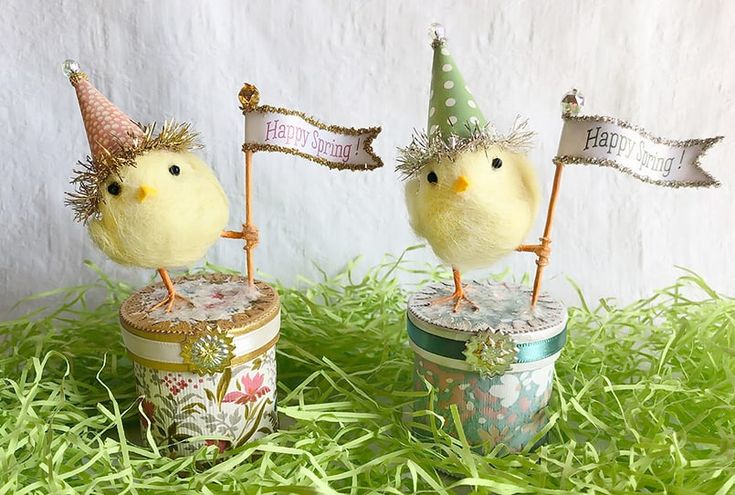 two small yellow birds wearing party hats on top of tin canisters in grass