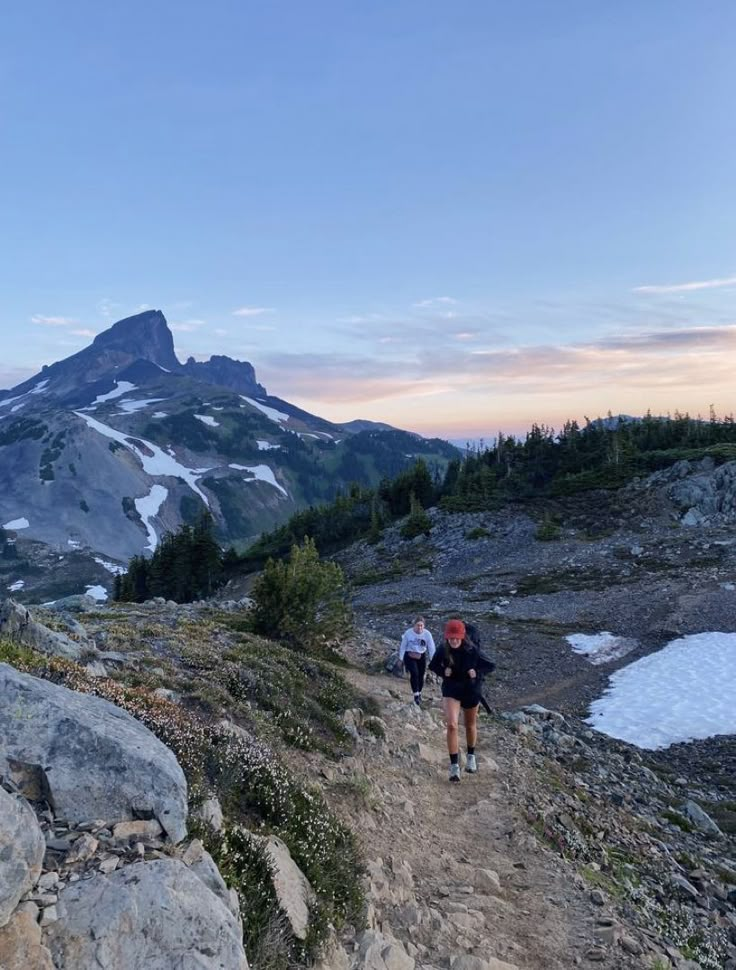 two people hiking up a trail in the mountains at sunset with snow on the ground