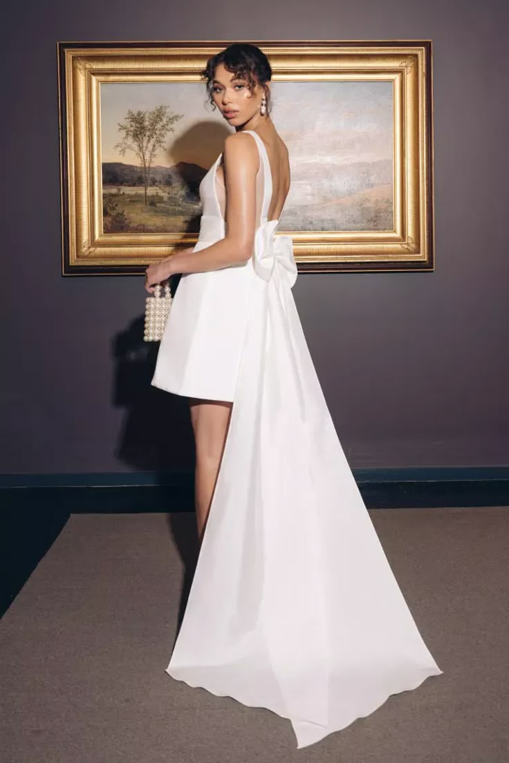 a woman standing in front of a painting wearing a white dress with high slits