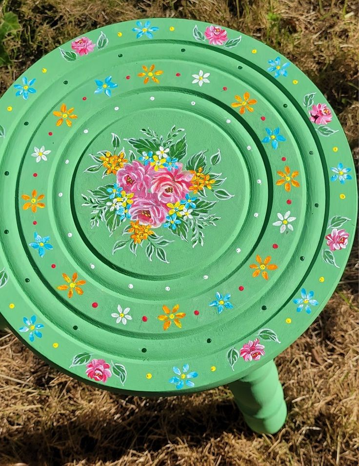 a green frisbee with flowers painted on it sitting in the middle of grass