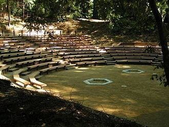 an outdoor seating area in the woods with benches and trees around it for people to sit on