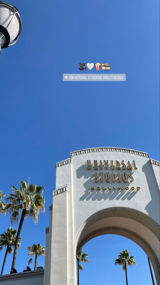 the entrance to universal studios hollywood with palm trees in the foreground and an overhead sign above it