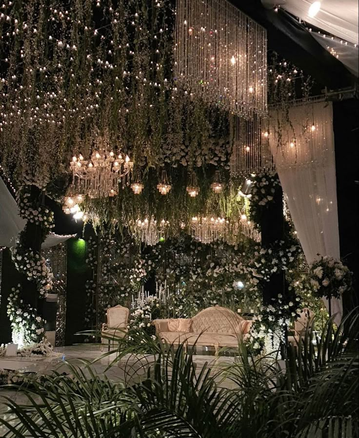 a room filled with lots of white flowers and greenery hanging from the ceiling next to a couch