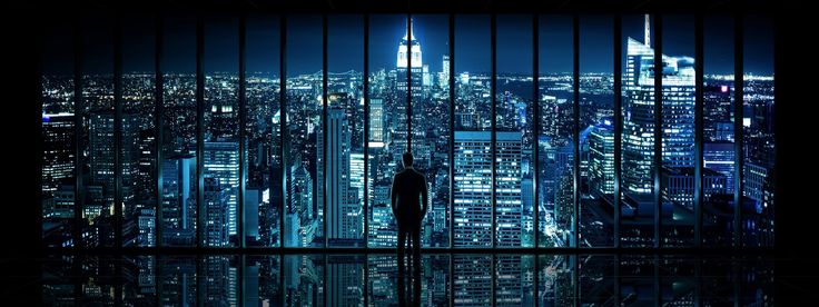 a man standing in front of a window looking out at the city lights and skyscrapers