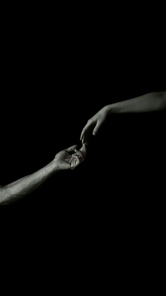 two hands reaching out towards each other in the dark with one hand holding the other's hand