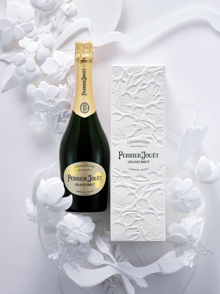 a bottle of champagne sitting next to a box on a white surface with flowers in the background