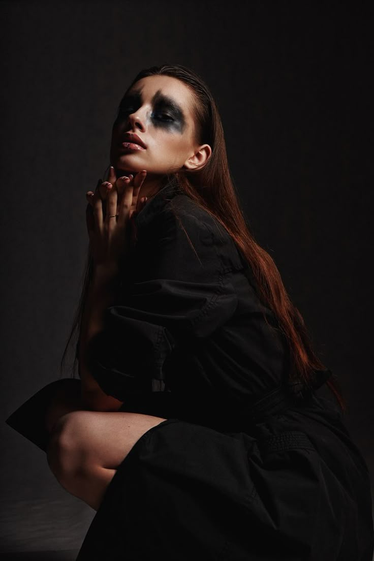 a woman with makeup on her face is sitting in the dark and posing for a photo